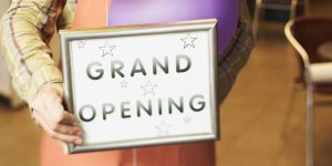 Someone holding a sign that reads "GRAND OPENING" for a franchise